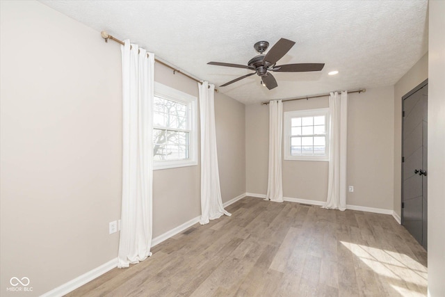 unfurnished room featuring ceiling fan, light hardwood / wood-style flooring, a textured ceiling, and plenty of natural light