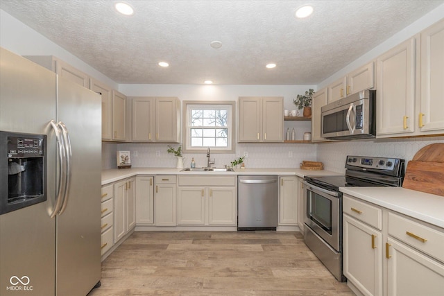 kitchen featuring sink, decorative backsplash, light hardwood / wood-style floors, stainless steel appliances, and a textured ceiling