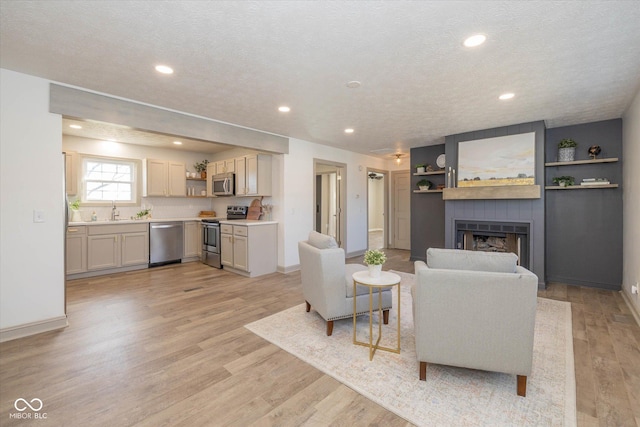 living room with sink, light hardwood / wood-style floors, a large fireplace, and a textured ceiling