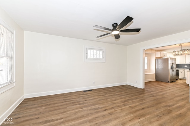 unfurnished living room with ceiling fan with notable chandelier and dark hardwood / wood-style flooring