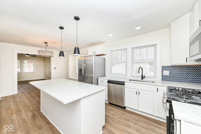 kitchen with pendant lighting, sink, appliances with stainless steel finishes, white cabinetry, and a kitchen island