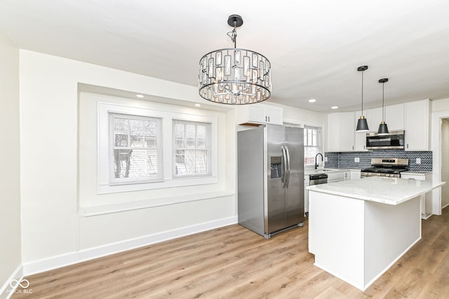 kitchen with appliances with stainless steel finishes, a kitchen island, white cabinetry, sink, and hanging light fixtures