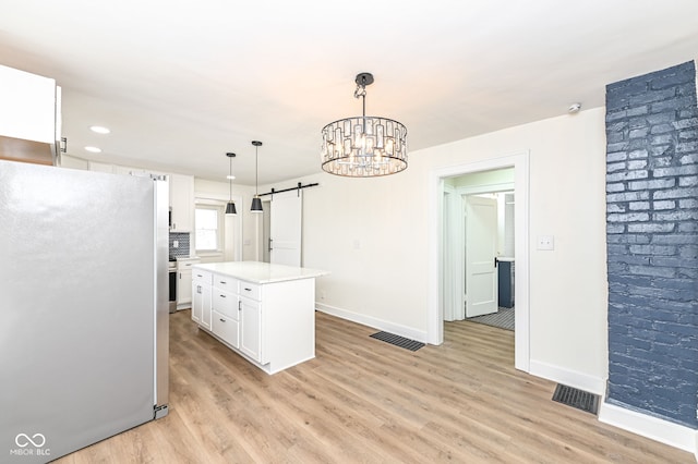 kitchen featuring pendant lighting, stainless steel refrigerator, white cabinetry, a center island, and a barn door