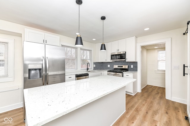 kitchen featuring pendant lighting, appliances with stainless steel finishes, white cabinetry, a center island, and light stone countertops