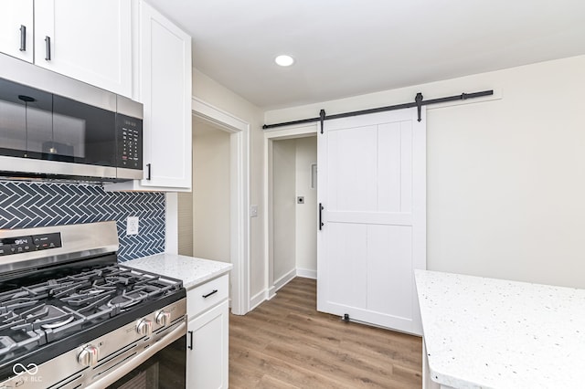 kitchen with stainless steel appliances, white cabinetry, a barn door, and light stone countertops