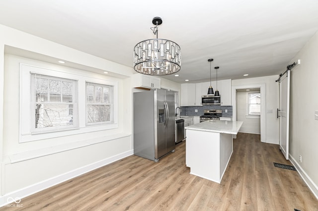 kitchen with stainless steel appliances, white cabinetry, a barn door, and hanging light fixtures