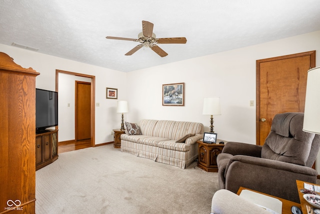 living room with ceiling fan, light carpet, and a textured ceiling