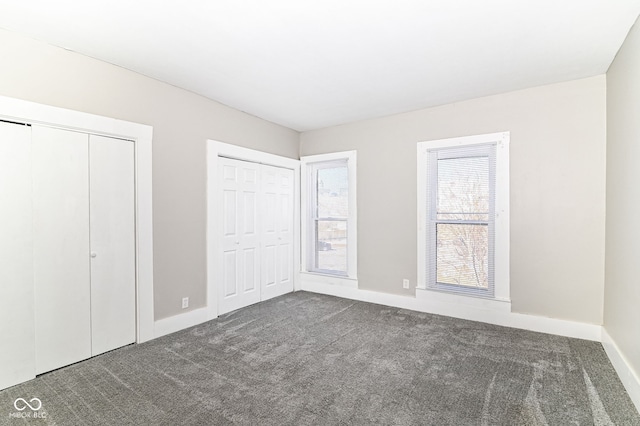 unfurnished bedroom with multiple closets, dark carpet, and baseboards