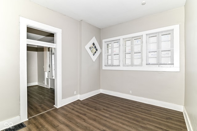 spare room featuring dark wood-style flooring, visible vents, and baseboards