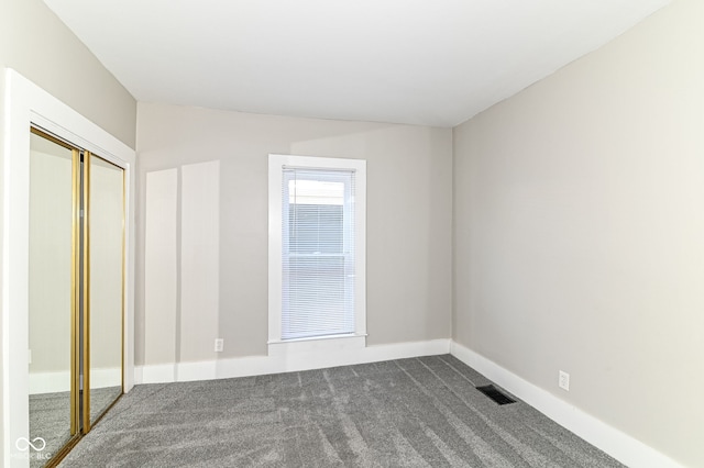 unfurnished bedroom featuring baseboards, visible vents, dark colored carpet, and a closet