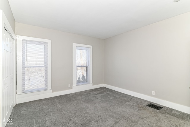 unfurnished room with dark carpet, visible vents, and baseboards