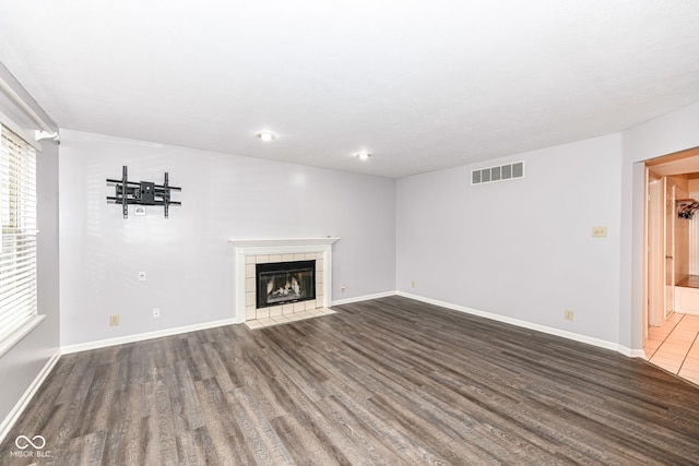 unfurnished living room featuring a tiled fireplace and dark hardwood / wood-style flooring