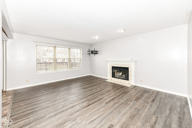 unfurnished living room featuring a tiled fireplace and dark wood-type flooring