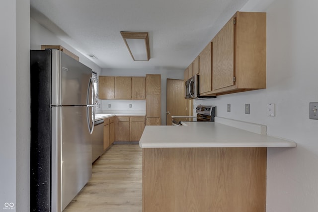 kitchen with light brown cabinetry, light hardwood / wood-style flooring, stainless steel appliances, and kitchen peninsula