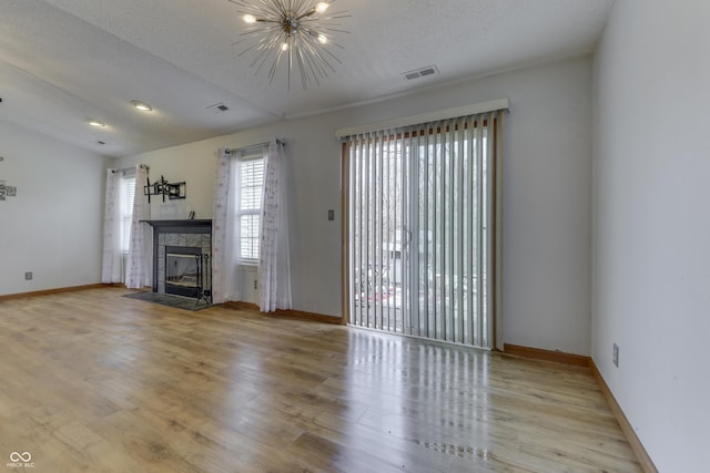 unfurnished living room with a fireplace, a chandelier, light hardwood / wood-style floors, and a textured ceiling