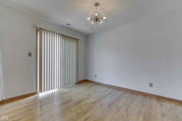 empty room featuring a notable chandelier, a textured ceiling, and light hardwood / wood-style flooring