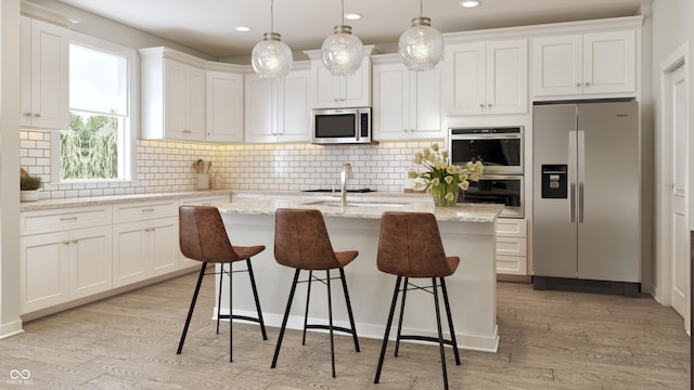 kitchen featuring decorative light fixtures, a kitchen island with sink, stainless steel appliances, light wood-type flooring, and white cabinetry