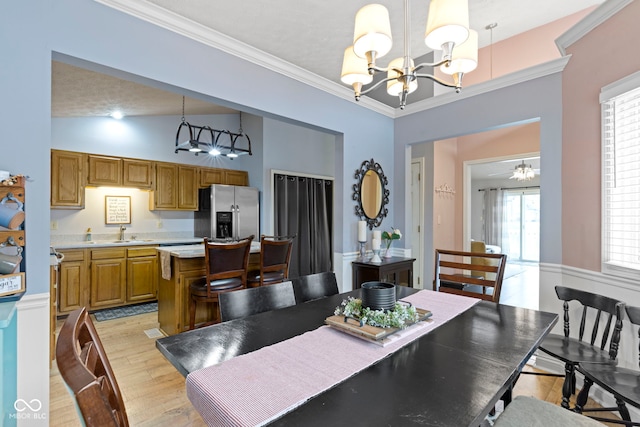 dining room with vaulted ceiling, sink, ornamental molding, a notable chandelier, and light wood-type flooring