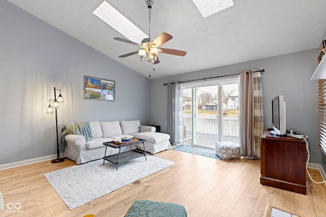 living room featuring vaulted ceiling with skylight, light hardwood / wood-style floors, and ceiling fan