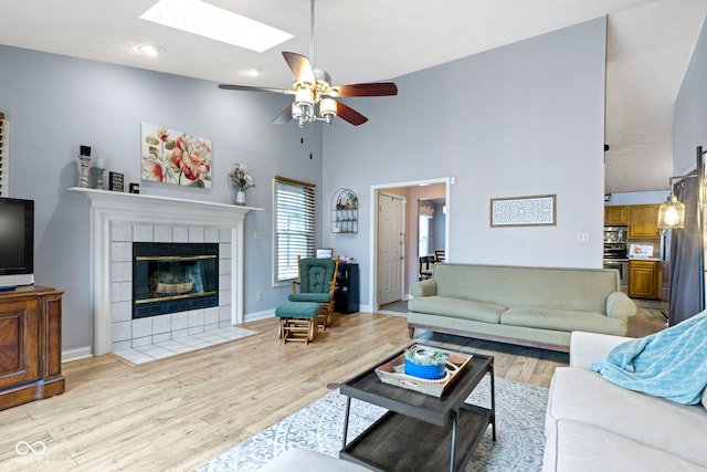 living room with a high ceiling, a tile fireplace, light wood-type flooring, and a skylight