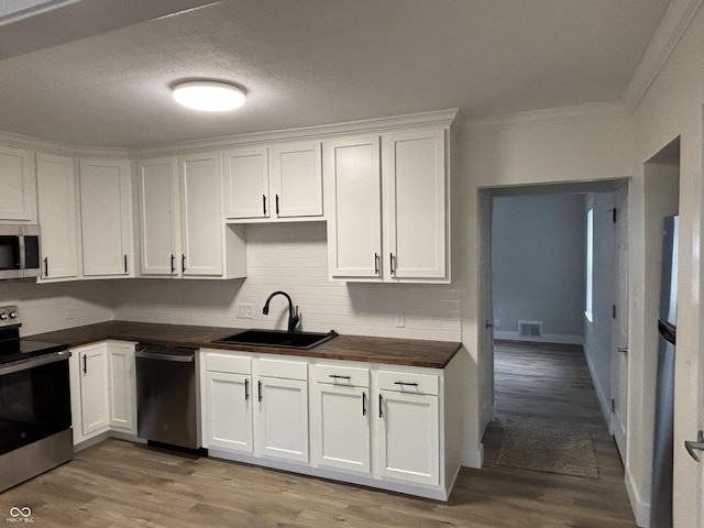 kitchen with sink, light wood-type flooring, ornamental molding, appliances with stainless steel finishes, and white cabinets