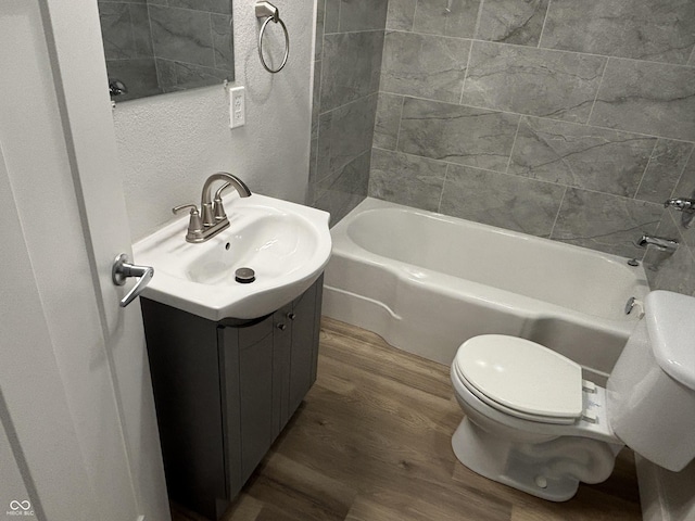 full bathroom with hardwood / wood-style flooring, vanity, tiled shower / bath, and toilet