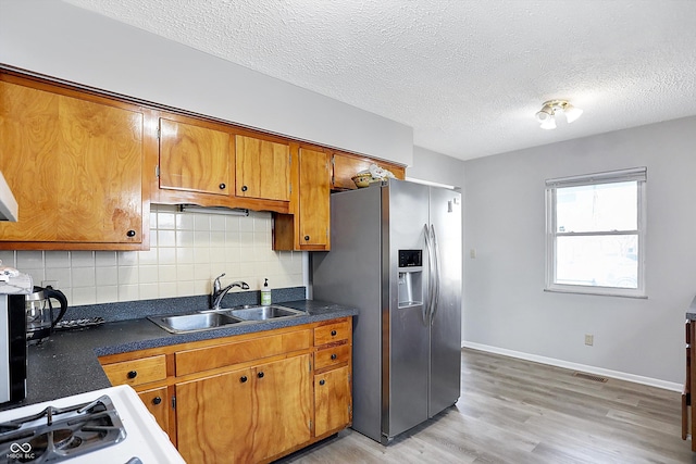 kitchen featuring sink, stainless steel refrigerator with ice dispenser, tasteful backsplash, a textured ceiling, and light wood-type flooring