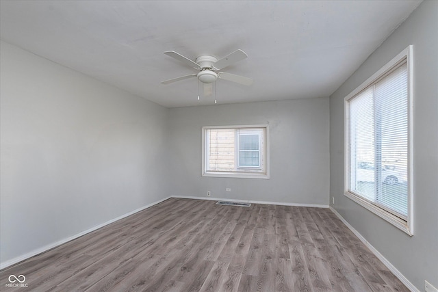 spare room with baseboards, wood finished floors, visible vents, and a healthy amount of sunlight