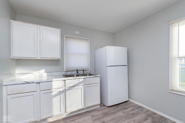 kitchen featuring freestanding refrigerator, a healthy amount of sunlight, white cabinetry, and a sink