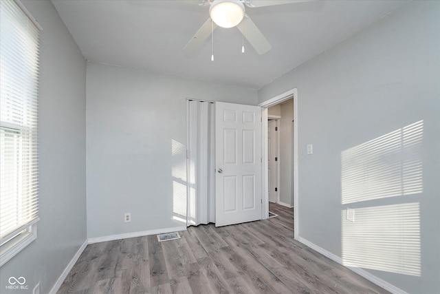 unfurnished bedroom featuring visible vents, multiple windows, baseboards, and wood finished floors