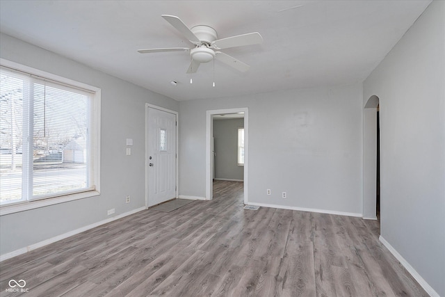 empty room with a ceiling fan, baseboards, arched walkways, and wood finished floors