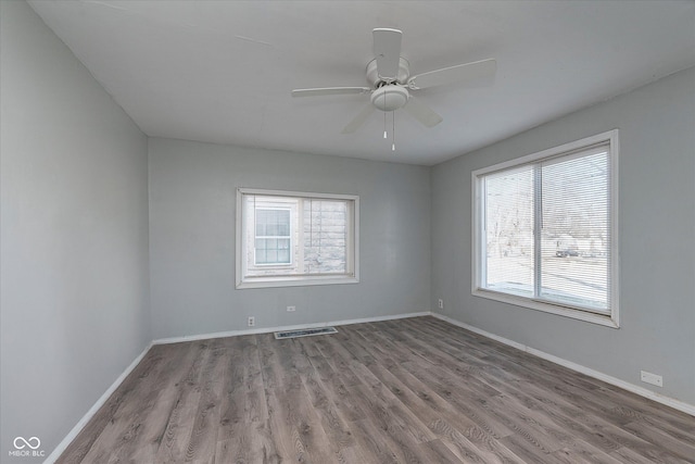 empty room with a ceiling fan, wood finished floors, visible vents, and baseboards