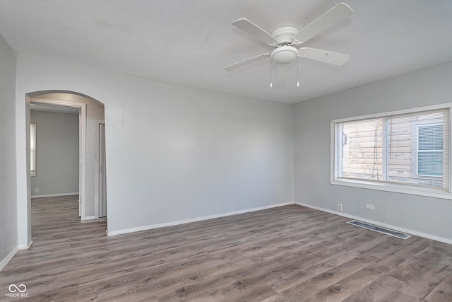 empty room featuring arched walkways, ceiling fan, wood finished floors, visible vents, and baseboards