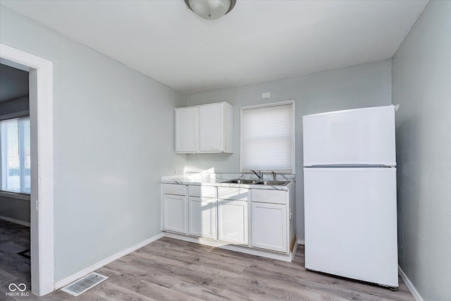 kitchen featuring light wood-type flooring, visible vents, a sink, and freestanding refrigerator