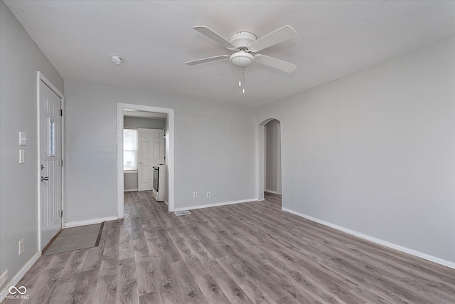 spare room with arched walkways, wood finished floors, visible vents, a ceiling fan, and baseboards