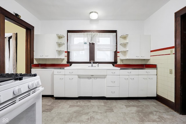 kitchen featuring white cabinetry, white gas range, sink, and tile walls