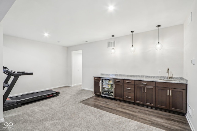 interior space featuring decorative light fixtures, sink, wine cooler, light stone countertops, and dark brown cabinets