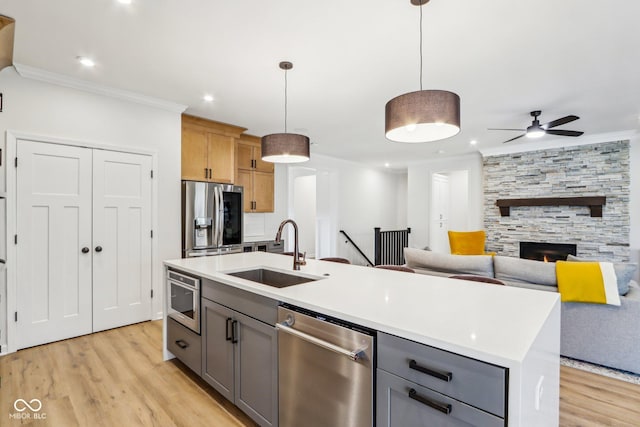 kitchen with appliances with stainless steel finishes, decorative light fixtures, sink, gray cabinetry, and a kitchen island with sink