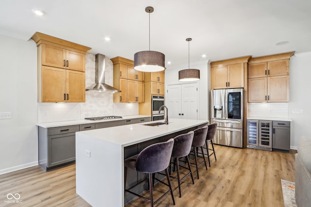 kitchen with wall chimney range hood, a breakfast bar, appliances with stainless steel finishes, an island with sink, and decorative light fixtures