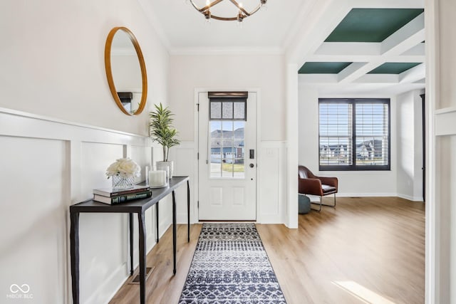 entryway featuring an inviting chandelier, crown molding, coffered ceiling, and light wood-type flooring