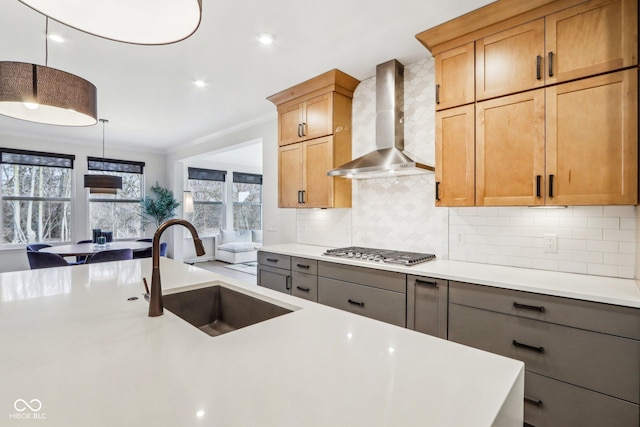 kitchen with wall chimney range hood, sink, tasteful backsplash, stainless steel gas cooktop, and decorative light fixtures