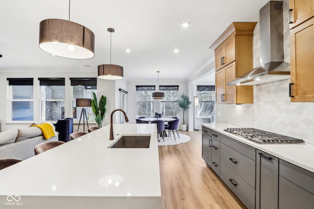 kitchen featuring hanging light fixtures, an island with sink, sink, and wall chimney exhaust hood