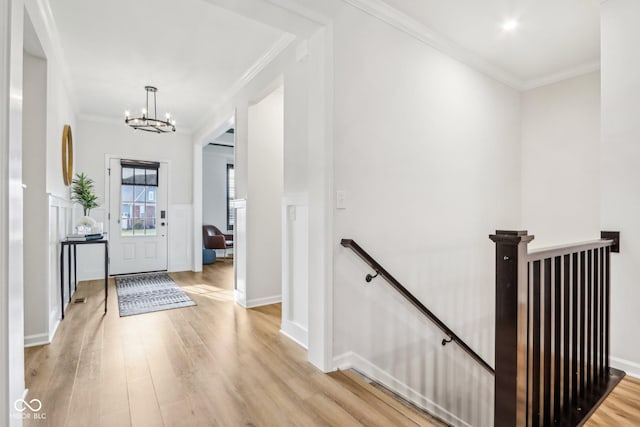 corridor with an inviting chandelier, ornamental molding, and light wood-type flooring