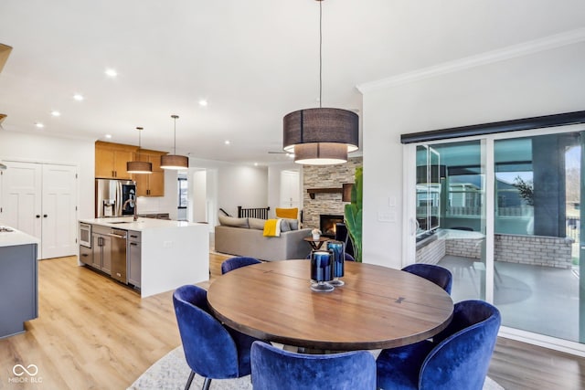 dining area with sink, a stone fireplace, ornamental molding, and light wood-type flooring