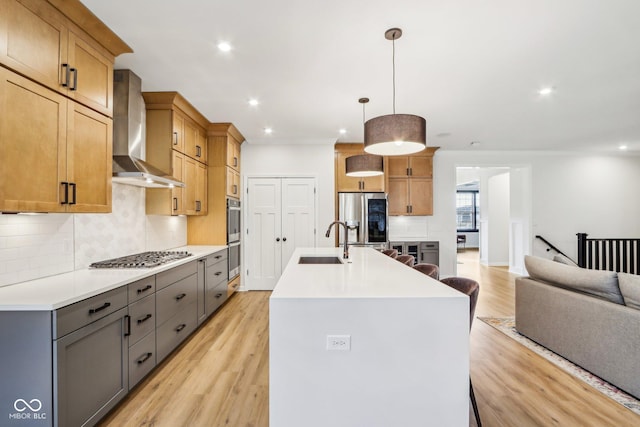 kitchen featuring a kitchen island with sink, decorative light fixtures, stainless steel appliances, and wall chimney exhaust hood