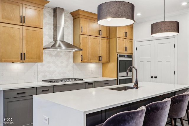 kitchen with stainless steel appliances, decorative light fixtures, a kitchen island with sink, and wall chimney range hood