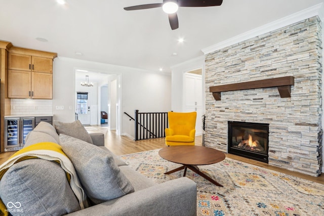 living room with light hardwood / wood-style flooring, ceiling fan, wine cooler, ornamental molding, and a stone fireplace