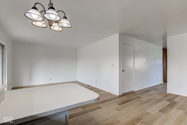 empty room with light wood-type flooring and an inviting chandelier