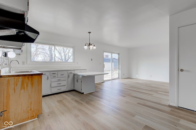 kitchen featuring light countertops, light wood-style floors, a chandelier, a sink, and exhaust hood