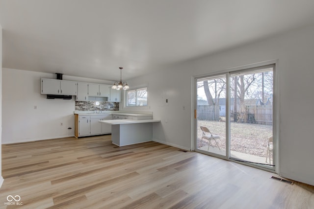 kitchen featuring white cabinetry, pendant lighting, light wood-type flooring, and kitchen peninsula